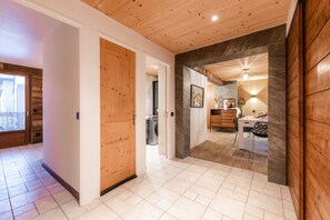 A hallway with wooden doors, a washing machine, a dining area with a table and chairs, and a stone wall. - Europa - Three Bedroom Apartment, Sleeps 8 (Briancon)