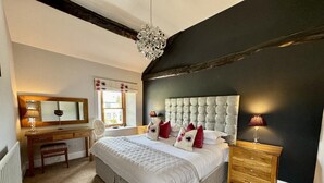 Een slaapkamer met een groot bed, een houten bureau, een stoel, een spiegel en een hanglamp.
