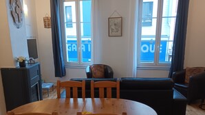 Ein Essbereich mit einem runden Holztisch, Stühlen, einer schwarzen Couch, einem Kamin und großen Fenstern mit Vorhängen.