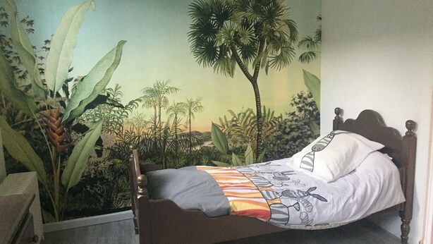 Ein Bett mit einer decke in ZEBRA-Muster, einer Wandmalerei von tropischen Pflanzen und einem hölzernen Kopfteil.