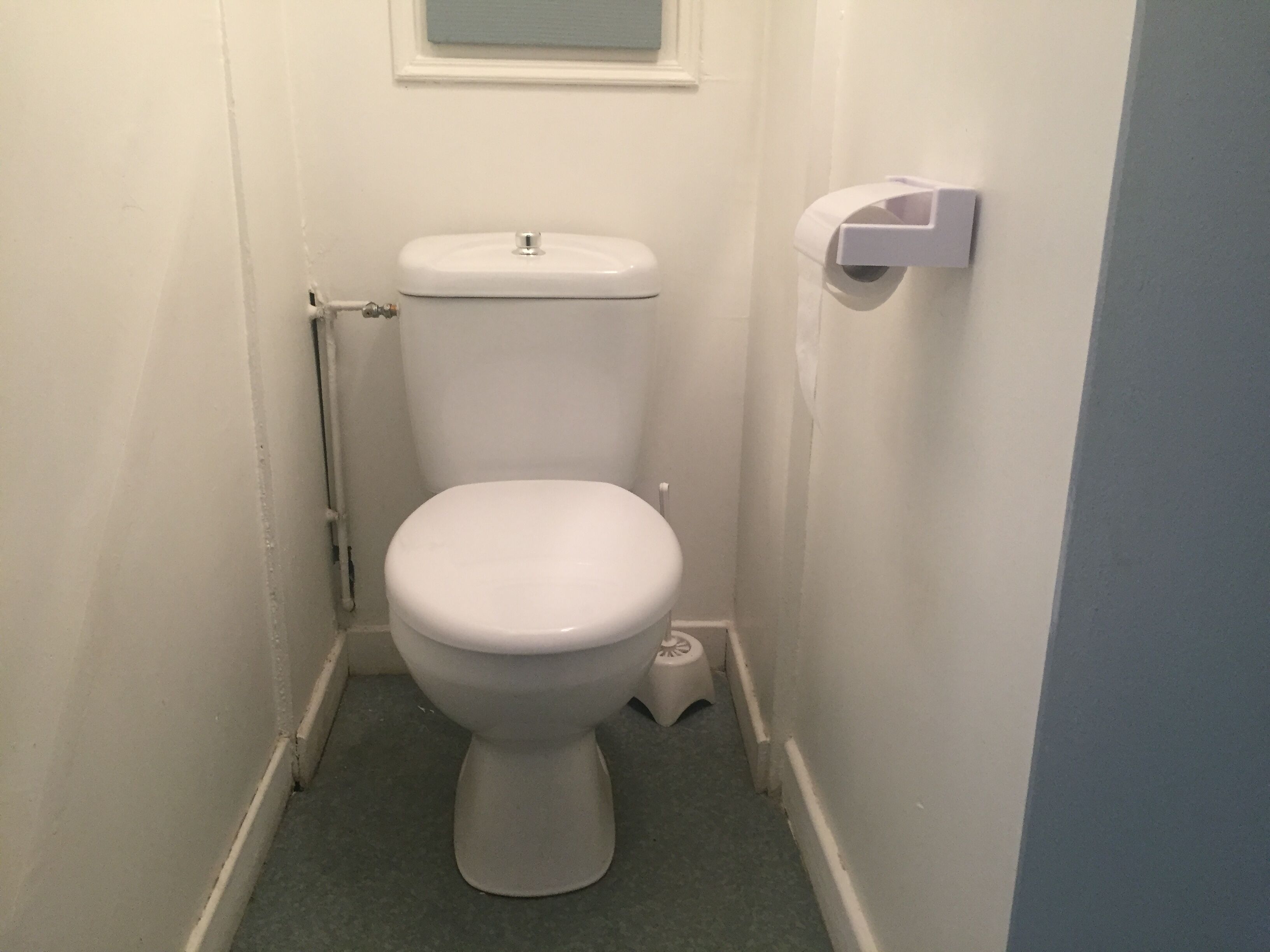 Eine kleine, weiße Toilette mit Tank, Papierhalter und einem kleinen Trittschemel daneben.