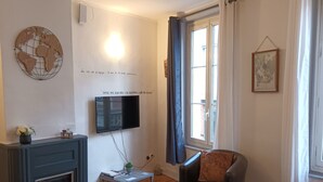 Ein Wohnzimmer mit Sofa, Couchtisch, Kamin, Fernseher und einem Fenster mit Vorhängen.