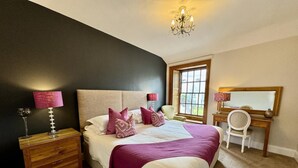 Un dormitorio con cama, mesitas de noche, escritorio, silla, ventana y candelabro.