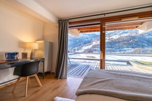 A bedroom with a bed, a desk, a chair, a lamp, and a view of snowy mountains. - Abela - Propriété d'exception, vue panoramique (Saint-Chaffrey)