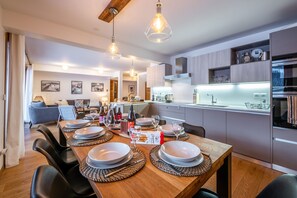A modern kitchen with a dining area set for four, featuring a wooden table, chairs, and a hanging light fixture. - Abela - Propriété d'exception, vue panoramique (Saint-Chaffrey)