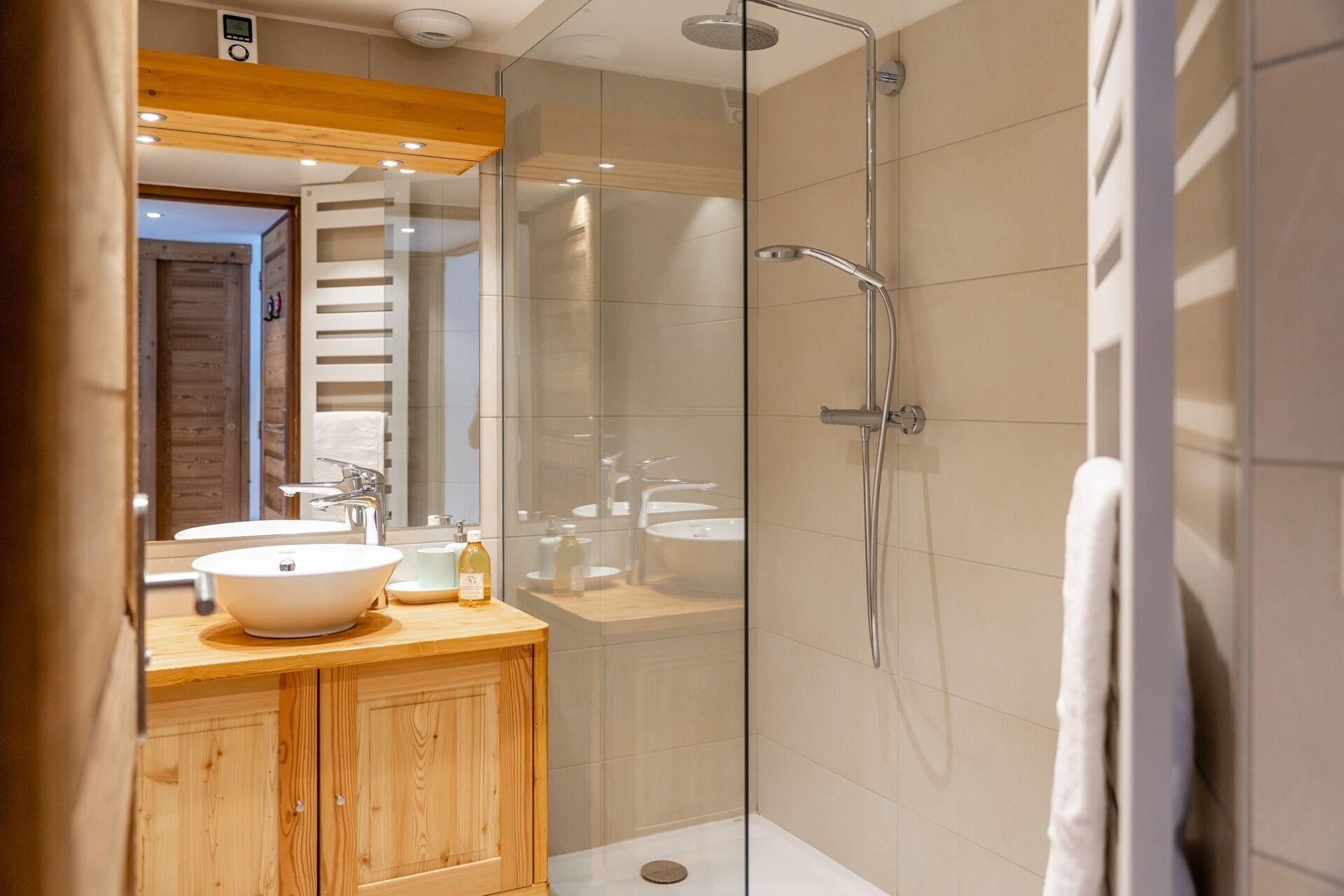 Un bagno moderno con cabina doccia in vetro, un mobile bagno in legno e uno specchio grande.