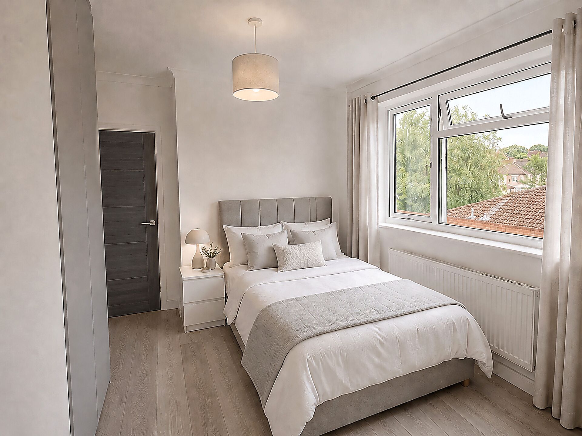 A bedroom with a bed, bedside tables, a lamp, a window with curtains, and a view of greenery outside.
