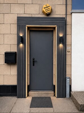 A modern security system sign above a dark door with a keypad and a doorbell. - Luxury 4-Bed Apartment (Northolt)
