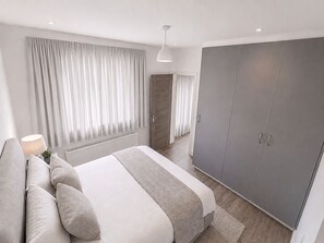 A modern bedroom with a bed, a wardrobe, and a nightstand. - Luxury 4-Bed Apartment (Northolt)