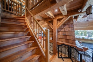 A wooden staircase with a railing, leading to a room with a stone wall and a view of the outdoors.