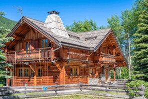 A wooden log cabin with a balcony, a chimney, and a fenced yard.