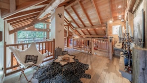 An interior with a high ceiling, wooden beams, a white chair, a table, and a guitar. - Echyllo - Six Bedroom Chalet, Sleeps 14 (Saint-Chaffrey)