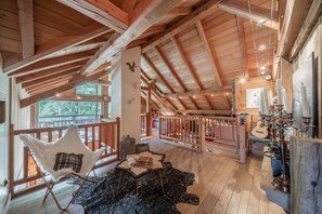 An interior with a high ceiling, wooden beams, a white chair, a table, and a guitar.