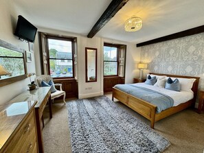 Een slaapkamer met een bed, een bureau, een stoel, een groot raam en een kroonluchter.
