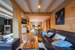 A cozy cabin interior with a wooden ceiling, a leather sofa, a dining area, and a fireplace.
