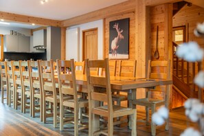 Ein Essbereich mit Holzbänken und Tisch, Holzwänden, einer Küche im Hintergrund und einer Holztreppe.