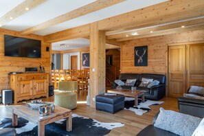 A wooden interior with a TV, sofa, ottoman, and dining area.