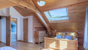 A wooden room with a sloped ceiling, a skylight, a bed, a dresser, and a bathroom with a bathtub. - Le Stam - Seven Bedroom House, Sleeps 15 (La Salle-les-Alpes)