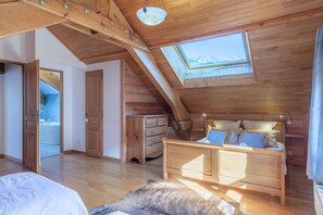 Ein Zimmer mit Holzboden und schrägem Dach, einem Oberlicht, einem Bett, einer Kommode und einem Badezimmer mit Badewanne.