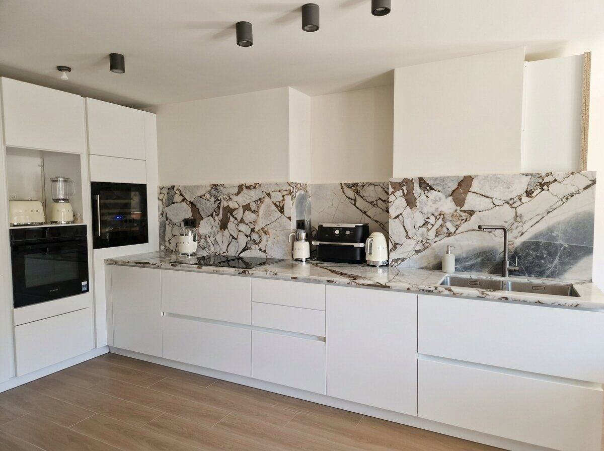 A modern kitchen with white cabinetry, a marble backsplash, and built-in appliances.