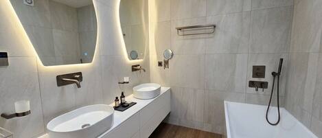 A modern bathroom with two sinks, a large mirror, a bathtub, and a shower.