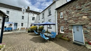 A courtyard with outdoor seating, stone buildings, and a door labeled 'Bridge Meadows.' - 1 Bed in Keswick (oc-b45234) (Keswick)