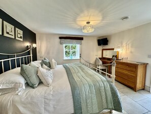 Ein Schlafzimmer mit Bett, Nachttisch, Kommode, Fernseher, Fenster und Kunstwerk an der Wand.