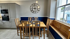 Una cocina con electrodomésticos integrados, una mesa de comedor con sillas, un reloj de pared y una ventana con vistas.