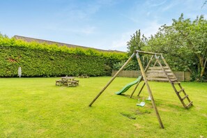 A backyard with a wooden swing set, a slide, and picnic tables. - 3 Bed in Keswick (oc-b45235) (Keswick)