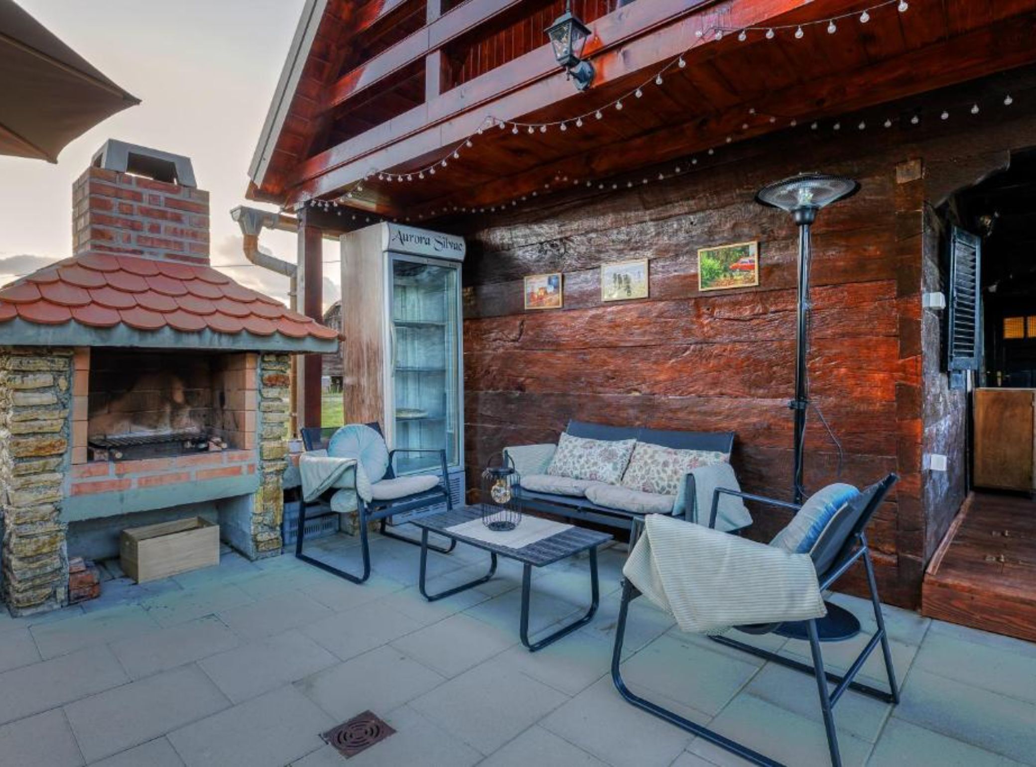 An outdoor patio with a brick fireplace, wicker furniture, and string lights.