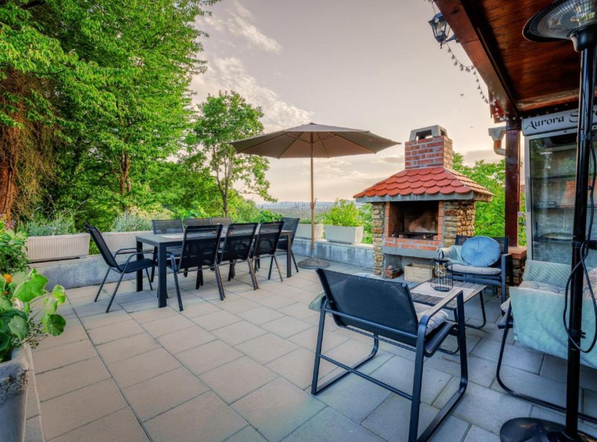 An outdoor patio with a brick fireplace, dining table, chairs, and an umbrella.