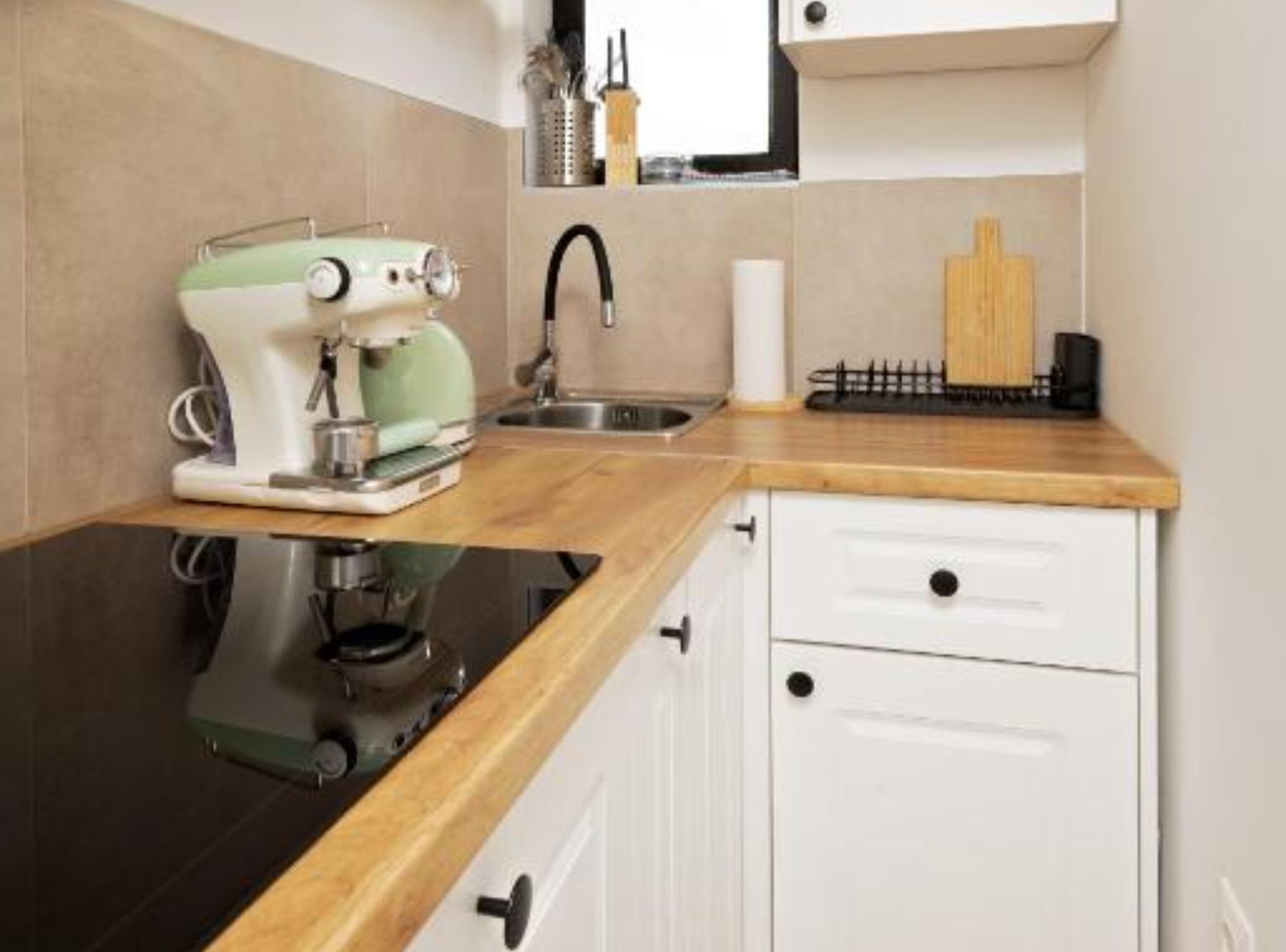 A kitchen with a coffee machine, a sink, a wooden countertop, and white cabinets.