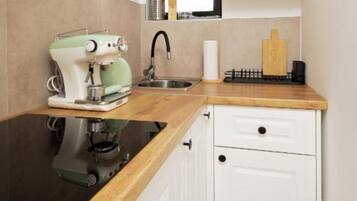A kitchen with a coffee machine, a sink, a wooden countertop, and white cabinets.
