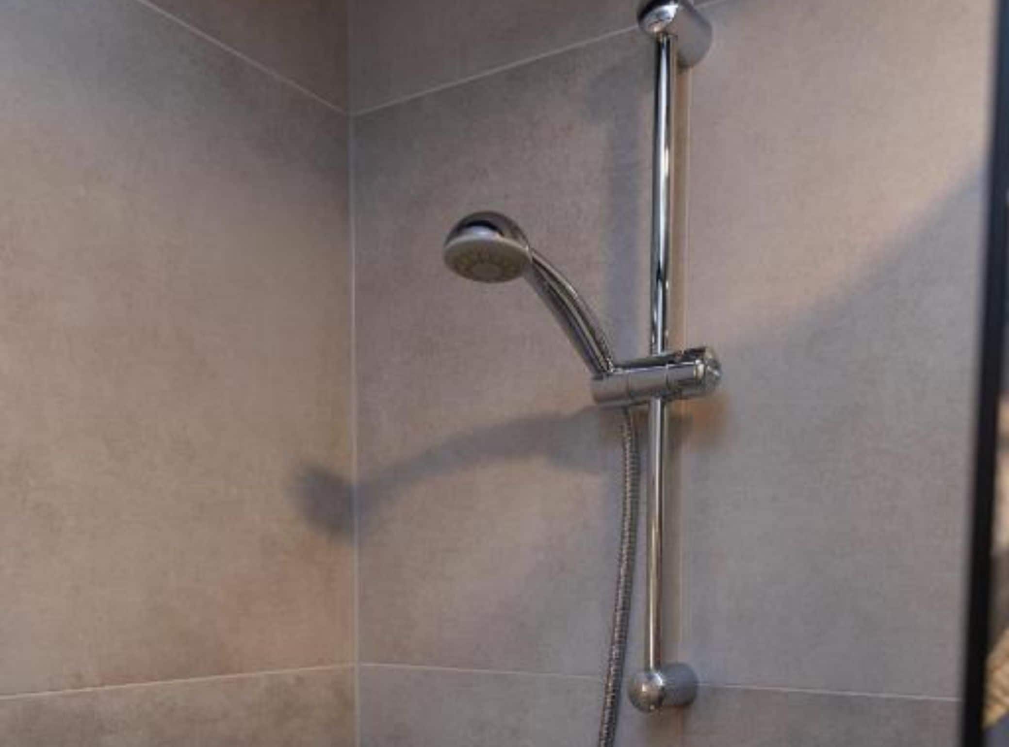 Une douche équipée d’un pommeau de douche à main et d’un robinet fixé au mur.
