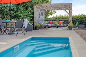 Ein Poolbereich mit Pergola, Sitzgelegenheiten im Freien und einem kleinen Pool.