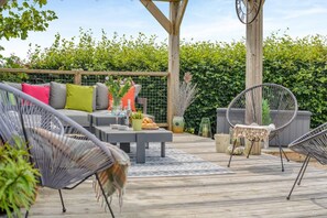 Eine Außenpatio mit Holzterrasse, Sitzbereich mit Stühlen und einer Couch, sowie einer Pergola.
