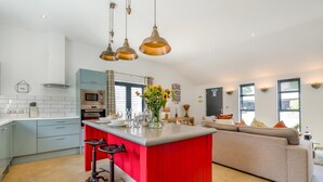 A modern kitchen with a red island, bar stools, and pendant lighting. - 2 Bed in West Putford (oc-u45226) (Sessacott)