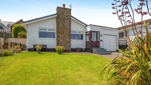 A single-story house with a stone chimney, a garage, and a well-maintained lawn. - 3 Bed in Bull Bay (oc-a45275) (Porth Llechog)