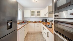 A modern kitchen with stainless steel appliances, white cabinetry, and a built-in oven. - 3 Bed in Bull Bay (oc-a45275) (Porth Llechog)