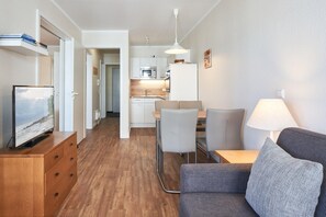 A compact living space with a kitchenette, a dining area, and a seating area with a TV and lamp. - Ferienwohnung Strandnah in Sellin mit Balkon und Wlan (Sellin)
