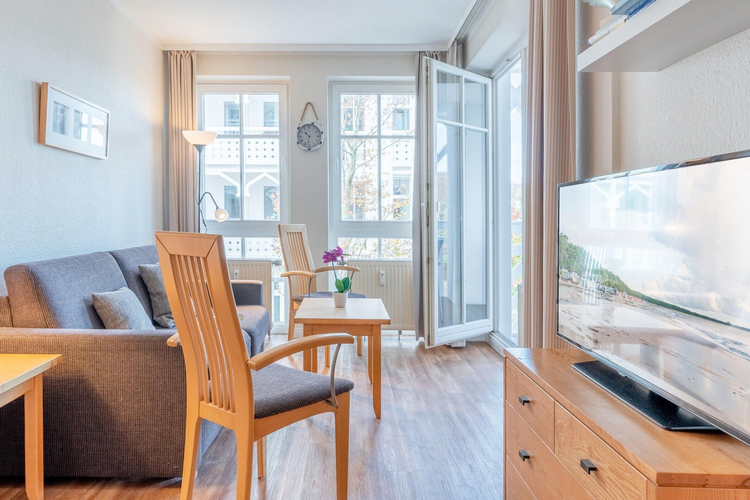 Un salon moderne avec un canapé, des chaises en bois, une table à manger, un téléviseur et de grandes fenêtres.