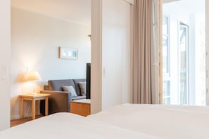 Een hotelkamer met een bed, een nachtkastje met een lamp, een sofa en een raam met gordijnen.