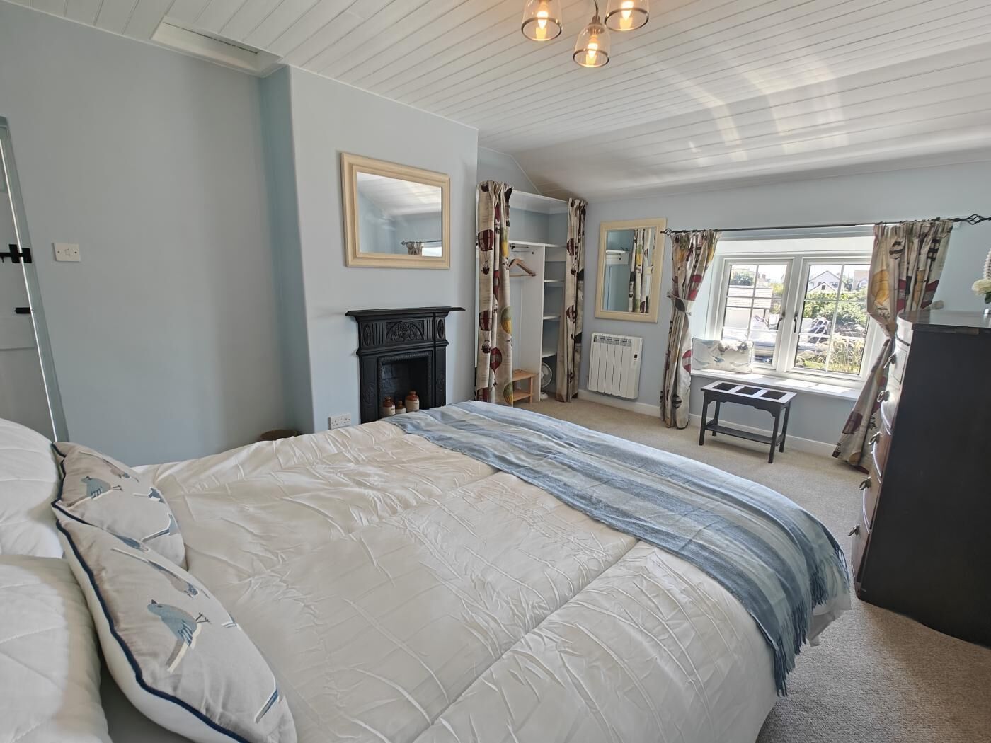 A bedroom with a bed, a fireplace, a window with curtains, and a mirror on the wall.