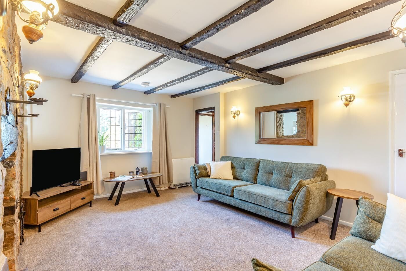 A living room with exposed wooden beams, a television, a sofa, and a small table.