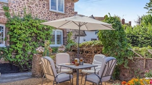 An outdoor patio with a table and chairs, surrounded by a stone wall and flowering plants. - 2 Bed in Carhampton (oc-v42711) (Carhampton)
