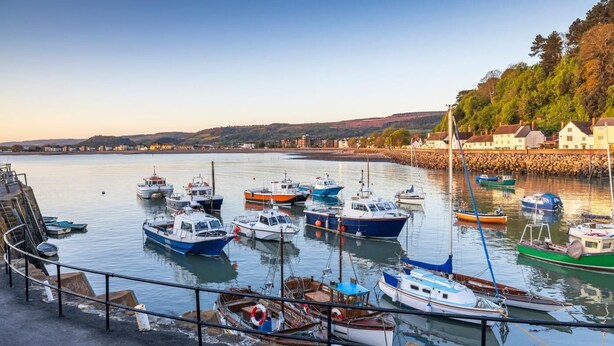 A harbor with various boats docked, a stone wall, and buildings in the background. - 2 Bed in Carhampton (oc-v42711) (Carhampton)