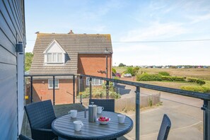 A balcony with a table set for two, overlooking a residential area with houses and a clear sky. - 2 Bed in Old Hunstanton (oc-b44902) (Hunstanton)