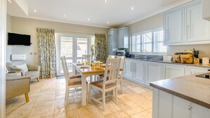 A spacious kitchen with a dining area, a television mounted above the seating, and a view through the glass doors. - 2 Bed in Old Hunstanton (oc-b44902) (Hunstanton)