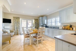A spacious kitchen with a dining area, a television mounted above the seating, and a view through the glass doors. - 2 Bed in Old Hunstanton (oc-b44902) (Hunstanton)