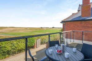 A balcony with a table, chairs, and a view of a golf course. - 2 Bed in Old Hunstanton (oc-b44902) (Hunstanton)